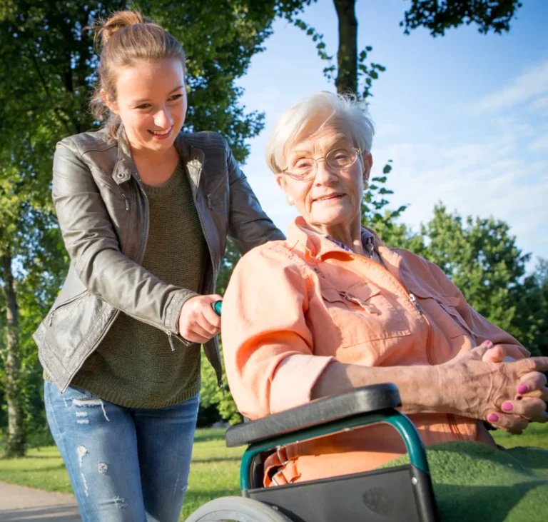 Junge Frau die Ihre Großmutter im Rollstuhl durch einen Park fährt.